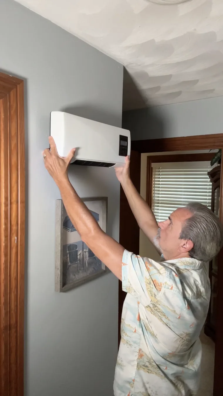 A man hanging the white heater on a bedroom wall